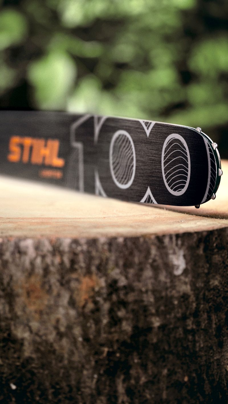 Schwarze STIHL-Schiene mit Jubil&auml;umsdesign liegt auf einem frisch ges&auml;gten Baumstumpf vor gr&uuml;nem Hintergrund