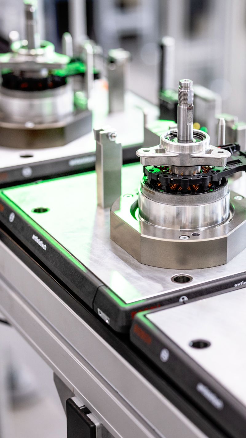 Pr&auml;zise montierte Baugruppe mit Metallgeh&auml;use und Kupferspulen steht auf moderner Produktionsanlage mit gr&uuml;nem Lichtsignal