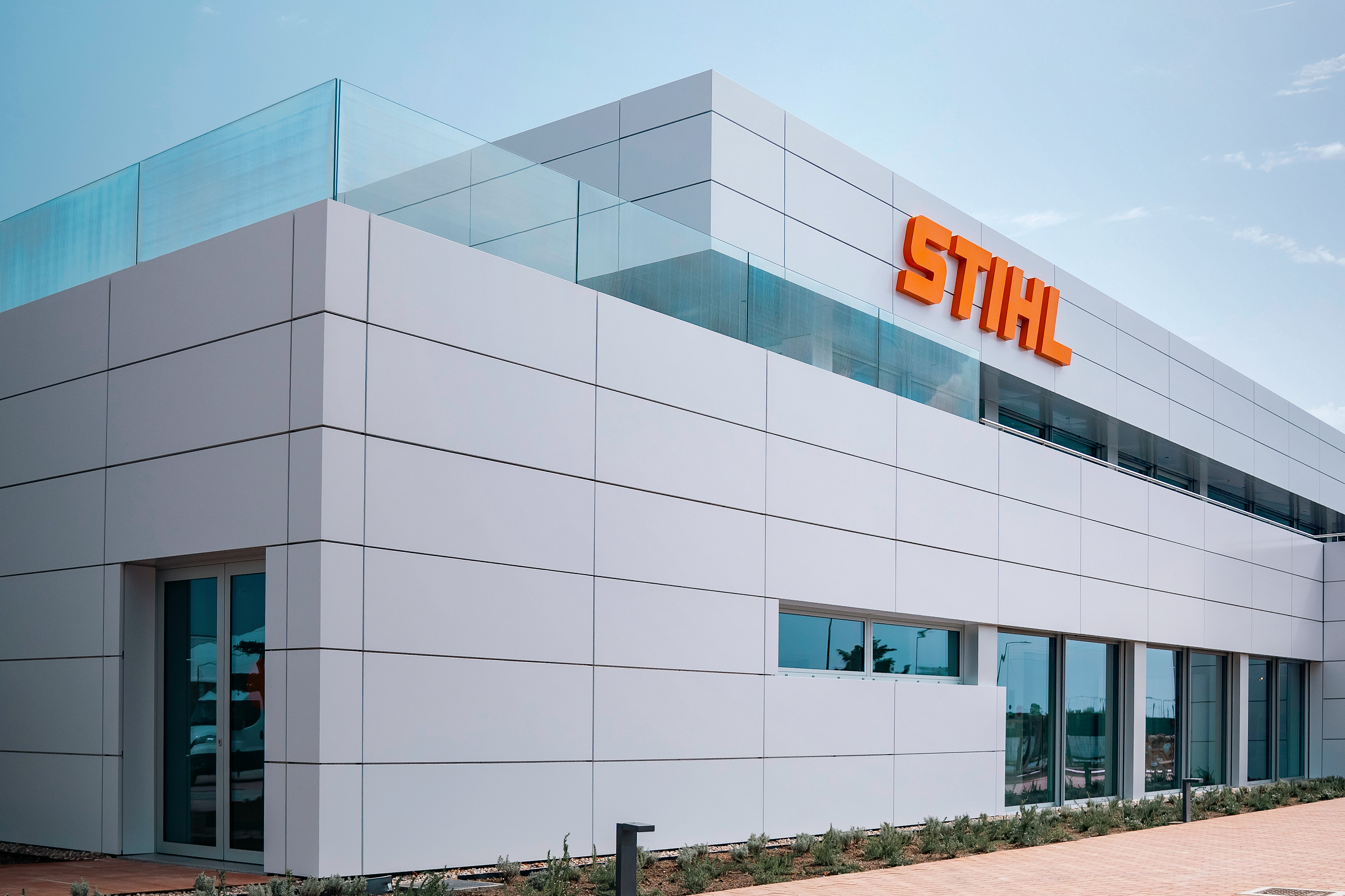 Modern STIHL building with white geometric facade, glass frontage and bright orange logo beneath a clear blue sky.