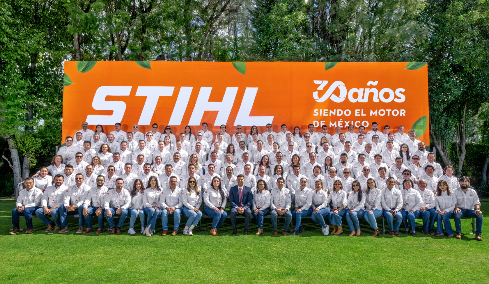  Large STIHL team group before orange 30 years anniversary wall in Mexico, all wearing white shirts, group photo on lawn