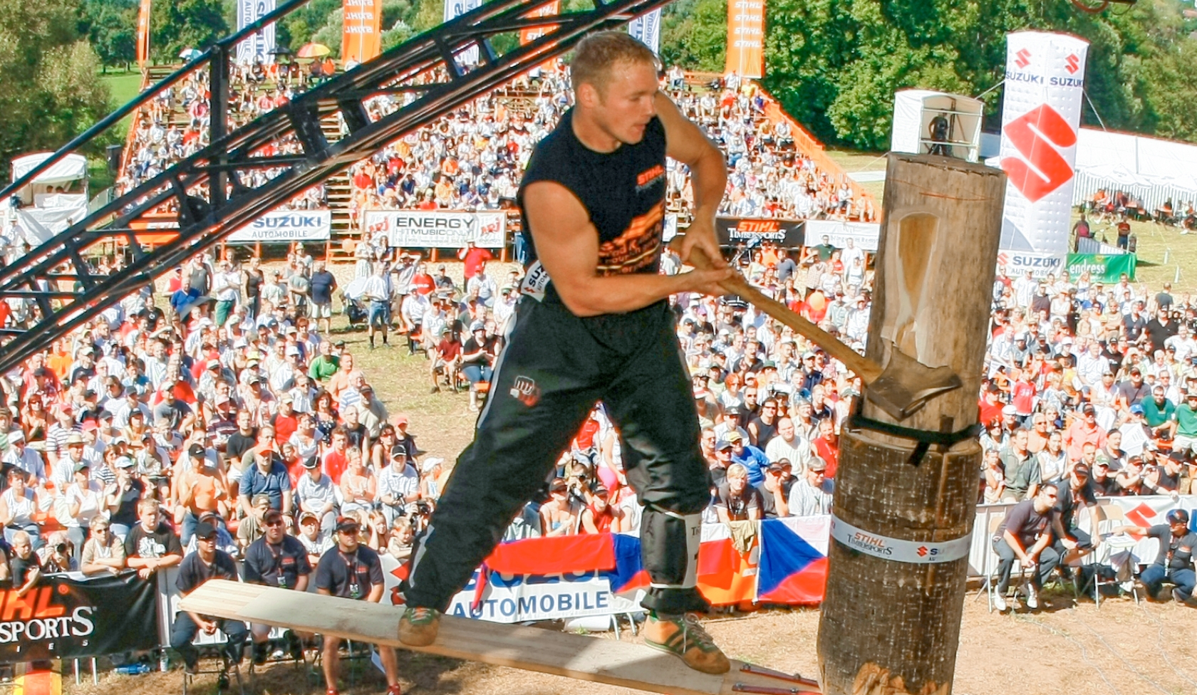 Athlete balancing on springboard board, swinging axe into upright log at STIHL Timbersports event before packed grandstand
