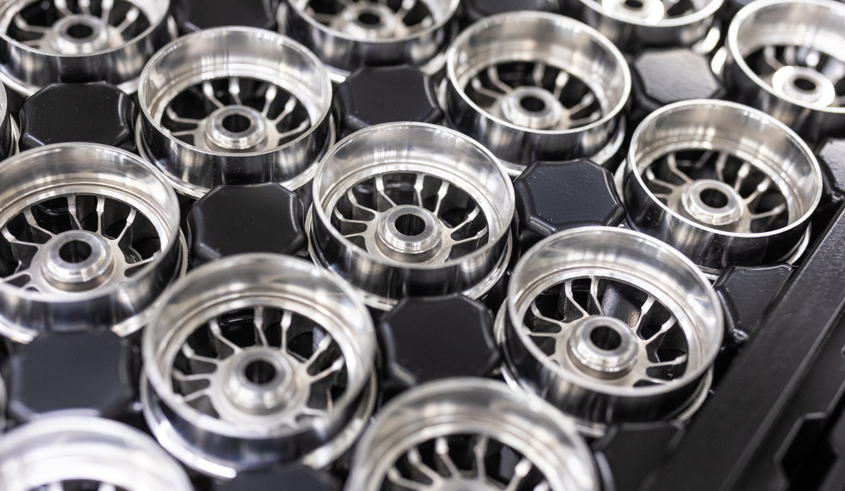 Multiple circular metal rotor parts with spoke design arranged in black carrier tray, prepared for electric motor assembly