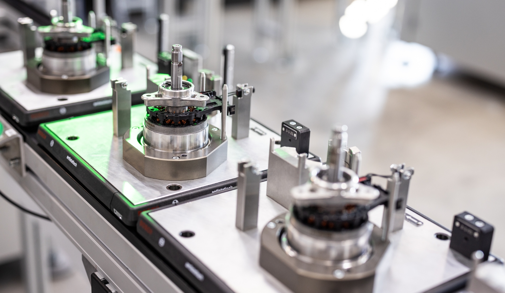 Assembly station with several clamped electric motors, metal housings and sensors, green illuminated test surface in foreground