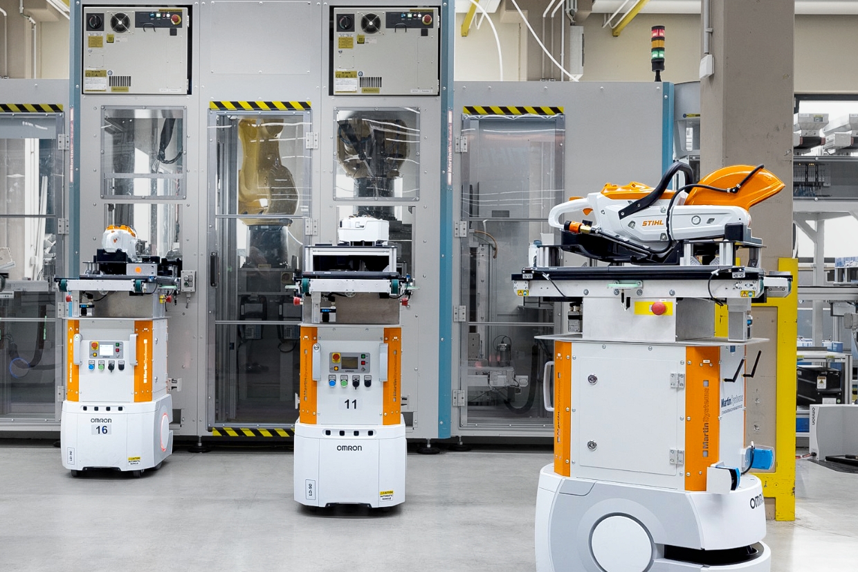 Several autonomous Omron transport robots carrying STIHL machines positioned before glassed production cell in modern factory