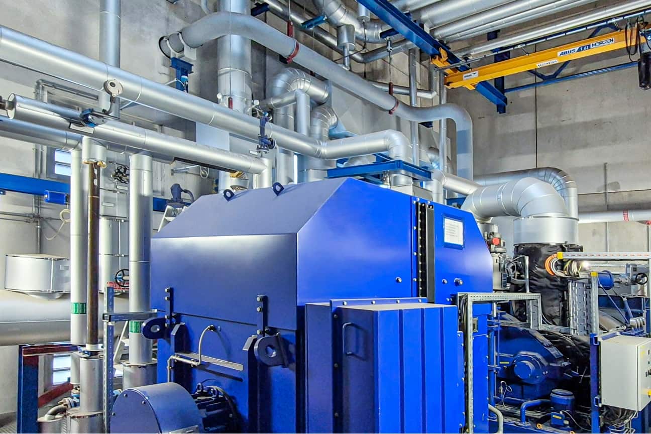 Interior of technical plant with large blue unit, many silver pipes and energy technology installed in industrial hall