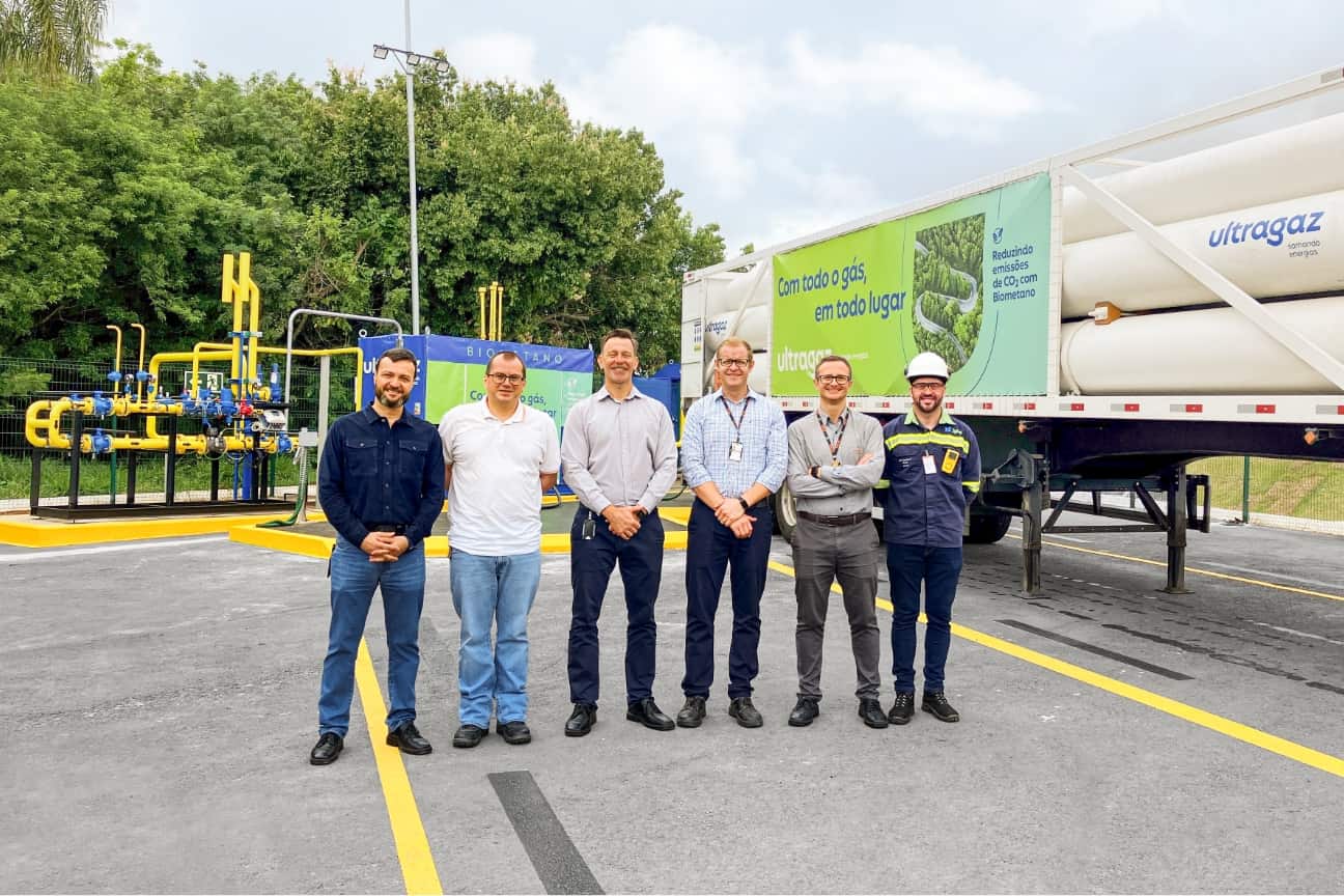 Six men standing before biogas installation and Ultragaz truck with biomethane slogan, yellow pipework and trees behind them
